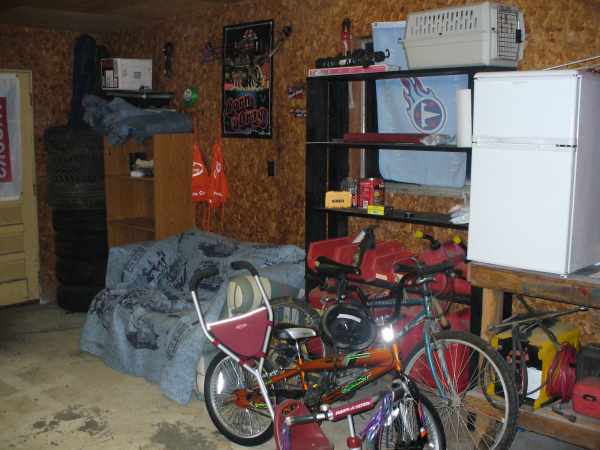 Garage interior with stacked tires, a bed, shelves with a refrigerator, and bicycles