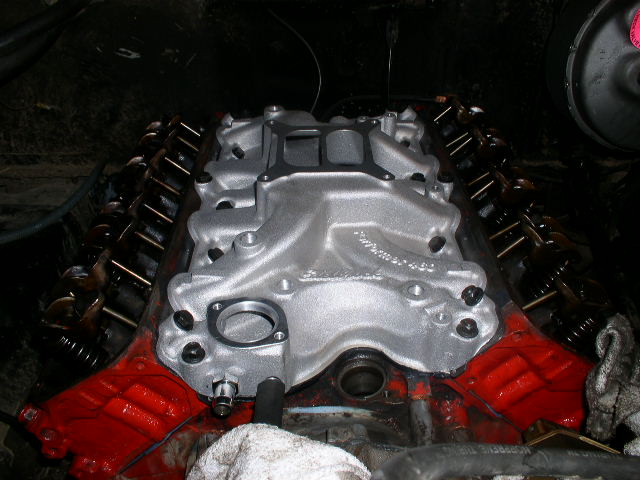 Bare aluminum intake manifold installed atop a V8 engine with red painted heads and exposed valvetrain