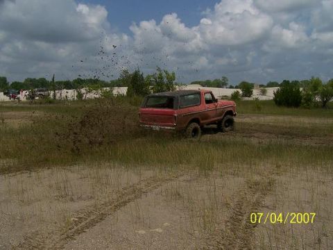 1978 Ford Bronco - A red 1978 Ford Bronco navigates a muddy terrain, sending dirt flying as it drives.