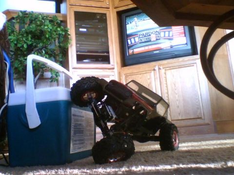 1993 Ford Bronco - A remote control car is seen tipped over on its side next to a cooler, with a television in the background.