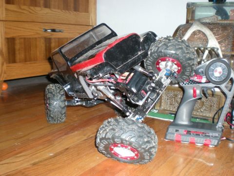 1993 Ford Bronco - A remote control rock crawler sits on a wooden floor next to its controller.