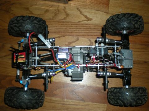 1993 Ford Bronco - The chassis of a remote control car is shown from a top-down perspective on a wooden floor.