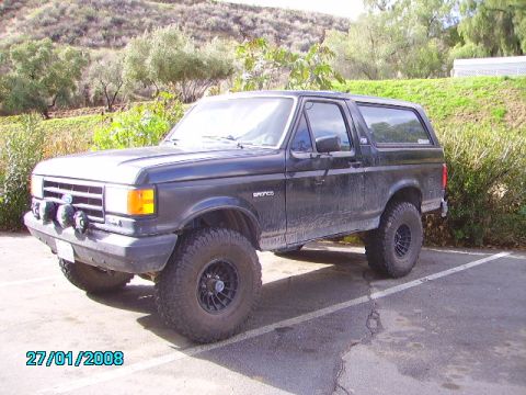 1990 Ford Bronco - A black 1990 Ford Bronco is shown from a three-quarter front angle in a parking lot.