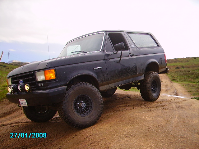 Black 1990 Ford Bronco with lifted suspension and off-road tires on a dirt path