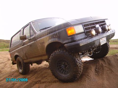 1990 Ford Bronco - This Ford Bronco is shown off-roading on a dirt hill, covered in mud.