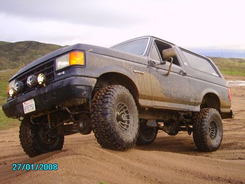 1990 Ford Bronco - A muddy 1990 Ford Bronco with large tires navigates a dirt track.
