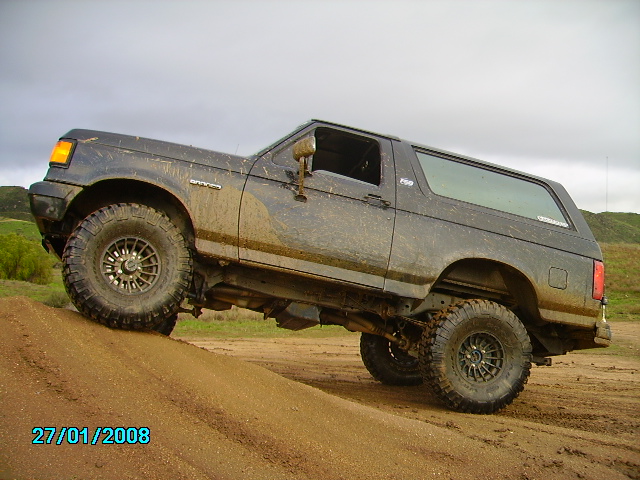 Muddy 1990 Ford Bronco climbing a dirt hill, side view