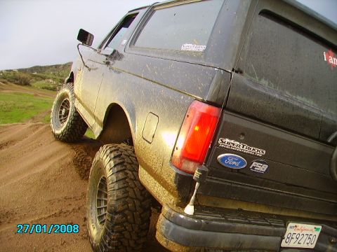 1990 Ford Bronco - Mud-covered 1990 Ford Bronco tackling an off-road trail.