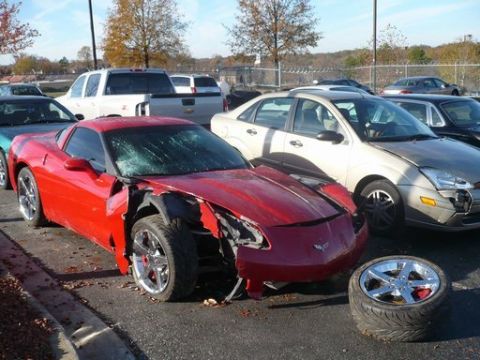 1979 Ford Bronco - A red sports car sits with significant front-end damage, its wheel detached and lying nearby.