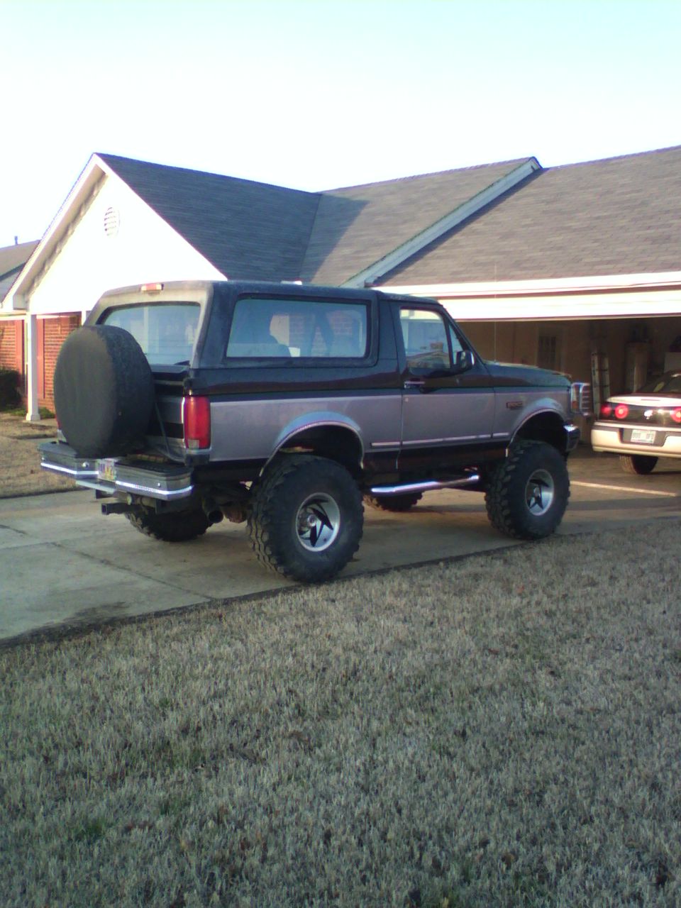 Lifted 1995 Ford Bronco parked in a driveway with a house in the background. Another car is visible in the garage