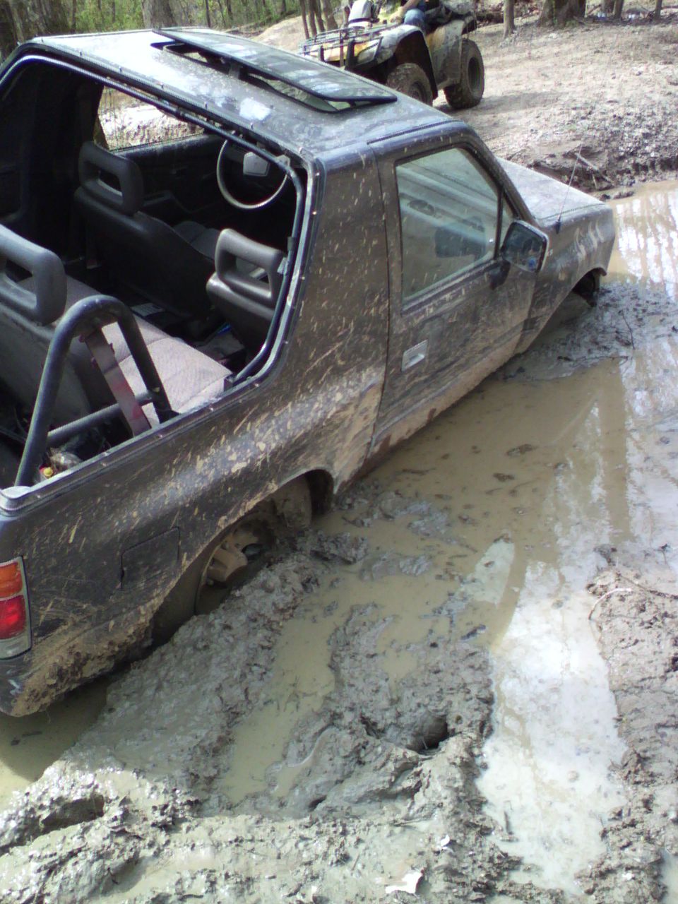 Topless mud-covered Isuzu stuck in a deep mud pit with an ATV behind it