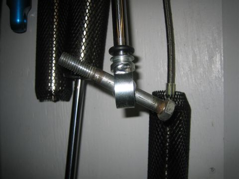1987 Suzuki Samurai - Close-up of a metal bracket assembly with a bolt and mesh sleeve, against a plain wall.