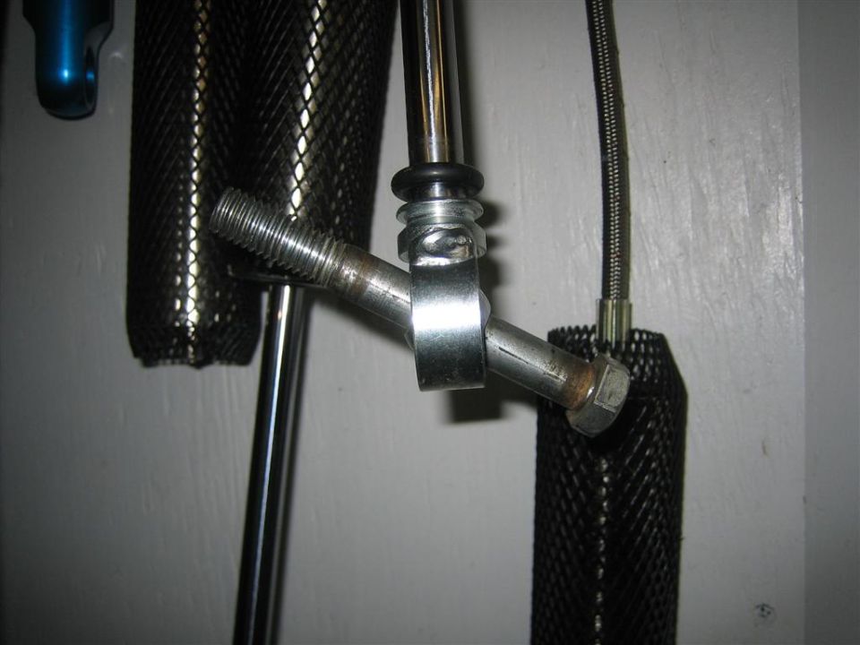 Metal bracket with bolt, rubber washer, and black mesh sleeve against a white wall