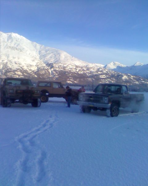 1990 Ford F-250 - Several trucks are parked in a snowy, mountainous area under a clear blue sky.