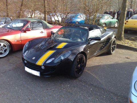 1991 Ford Crown Victoria - A black Lotus Elise convertible with yellow stripes is parked next to a red convertible sports car.