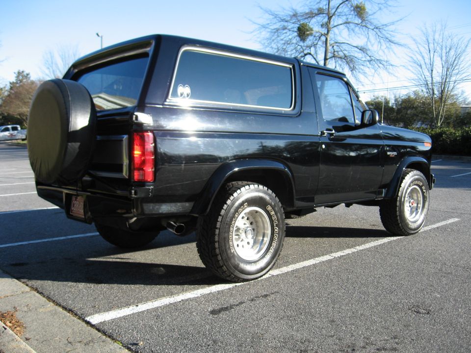 Black Ford Bronco SUV, rear three-quarter view, spare tire cover on tailgate, parked in a lot