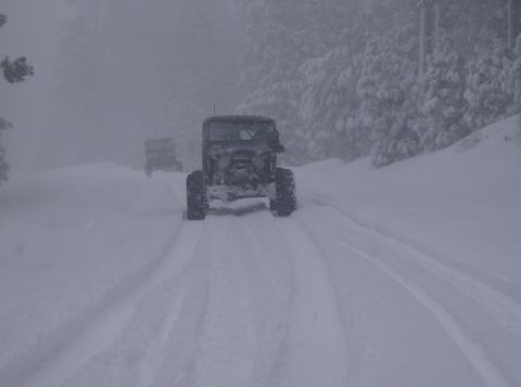 1986 Ford Bronco - Two off-road vehicles navigate a snowy road during a snowstorm.
