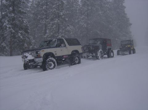1986 Ford Bronco - Multiple off-road vehicles navigate a snow-covered path during a snowfall.