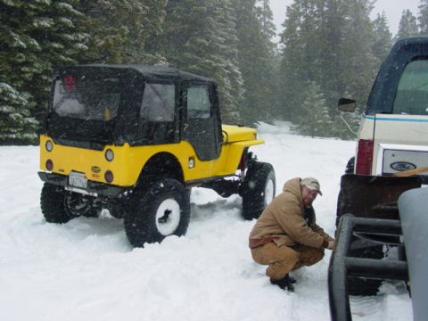 1986 Ford Bronco - A man works on a trailer in the snow next to a yellow Jeep and a Ford Bronco.