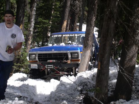 1979 Ford Bronco - A blue 1979 Ford Bronco is partially obscured by trees and snow, showing its front grille and winch.