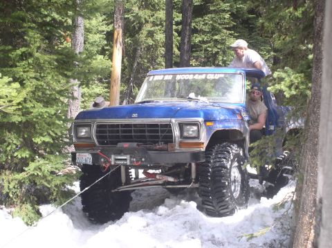 1979 Ford Bronco - Blue Ford Bronco with winch and two people navigates snowy terrain.