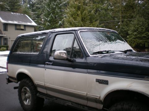 1993 Ford Bronco - A two-tone 1993 Ford Bronco is parked outside with snow dusting its windshield and roof.