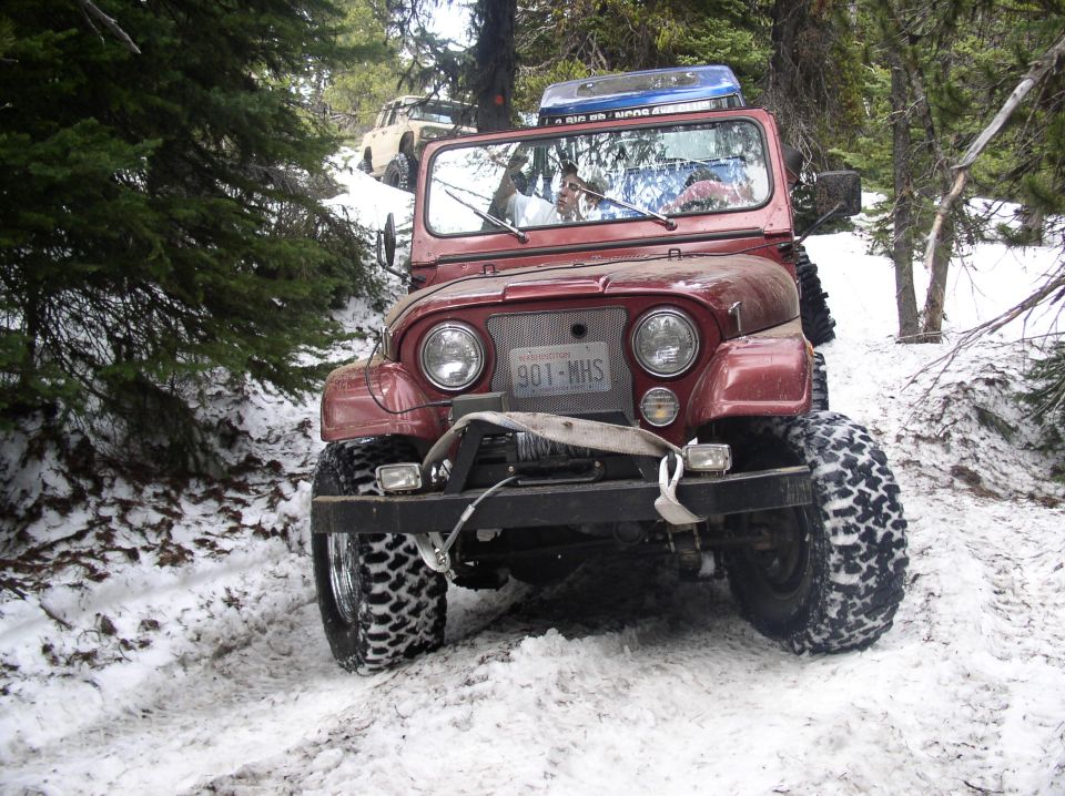 Maroon Jeep CJ with lift, mud tires and front bumper sitting on a snowy forest trail