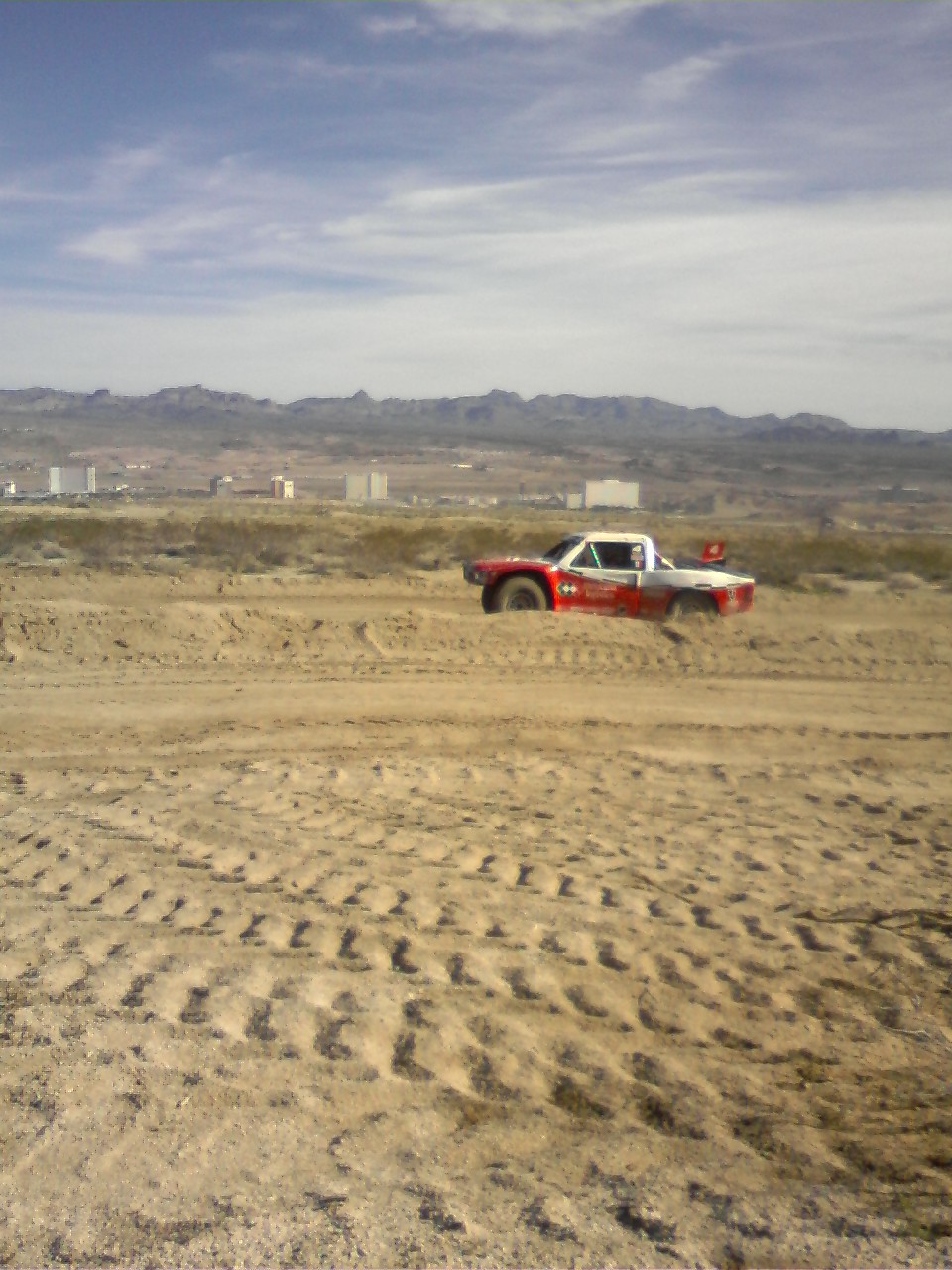 Red and white off-road vehicle with a roll cage, partially submerged in sand, with tire tracks visible
