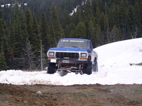 1979 Ford Bronco - Blue 1979 Ford Bronco navigates a snowy trail with a forest backdrop.