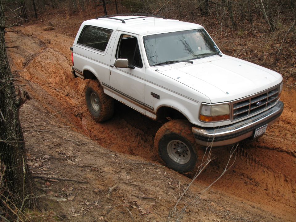White lifted Ford Bronco on muddy off-road trail in the woods