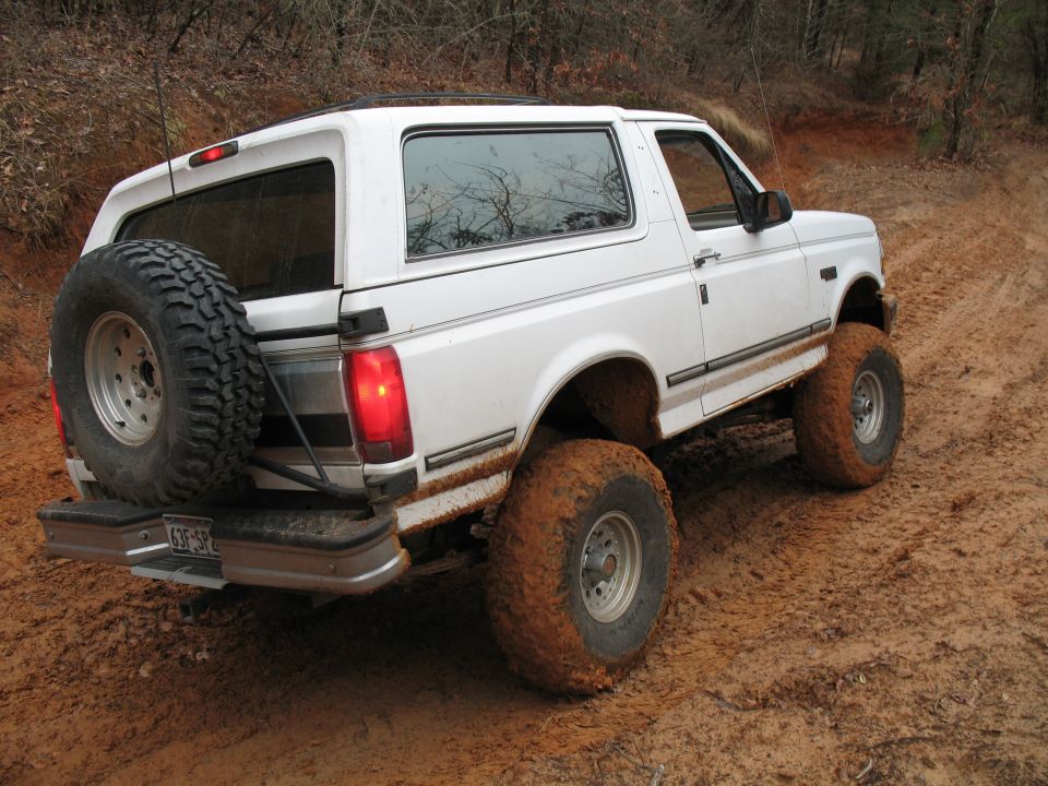White lifted Ford Bronco on mud tires off-road, rear three-quarter view