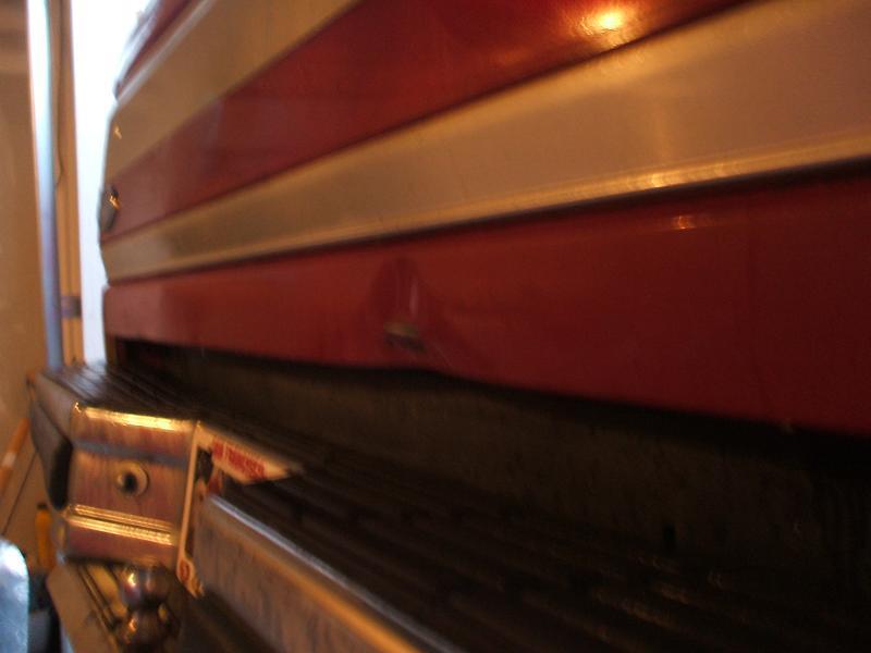 close-up of a red and silver vehicle's rear bumper and lower body panel with a small dent