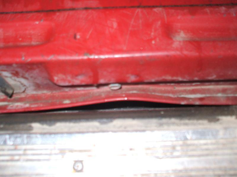 Close-up of a red car door's lower edge, showing a slight dent and a clip. Supermotors.net logo visible
