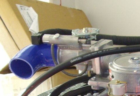 1985 Ford Bronco - A close-up view of engine components, including a blue silicone hose and a metal assembly with a dial.