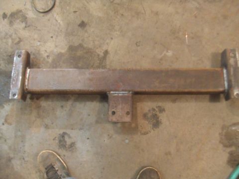 1996 Ford Bronco - A rusty metal frame with mounting brackets lies on a concrete floor, possibly a vehicle part.