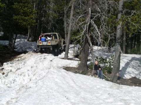 1979 Ford Bronco - A person sits by a tree while a tan pickup truck navigates a snowy incline.