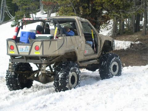 1979 Ford Bronco - This heavily modified off-road vehicle navigates a snowy terrain, equipped with large tires and a flatbed cargo area.