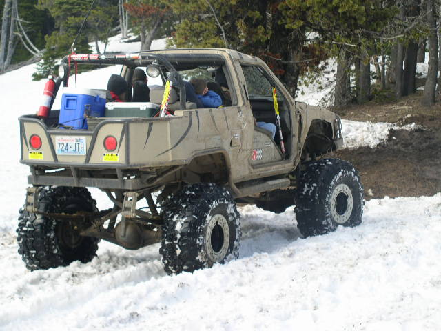 Tan off-road vehicle with large tires and a flatbed in the snow