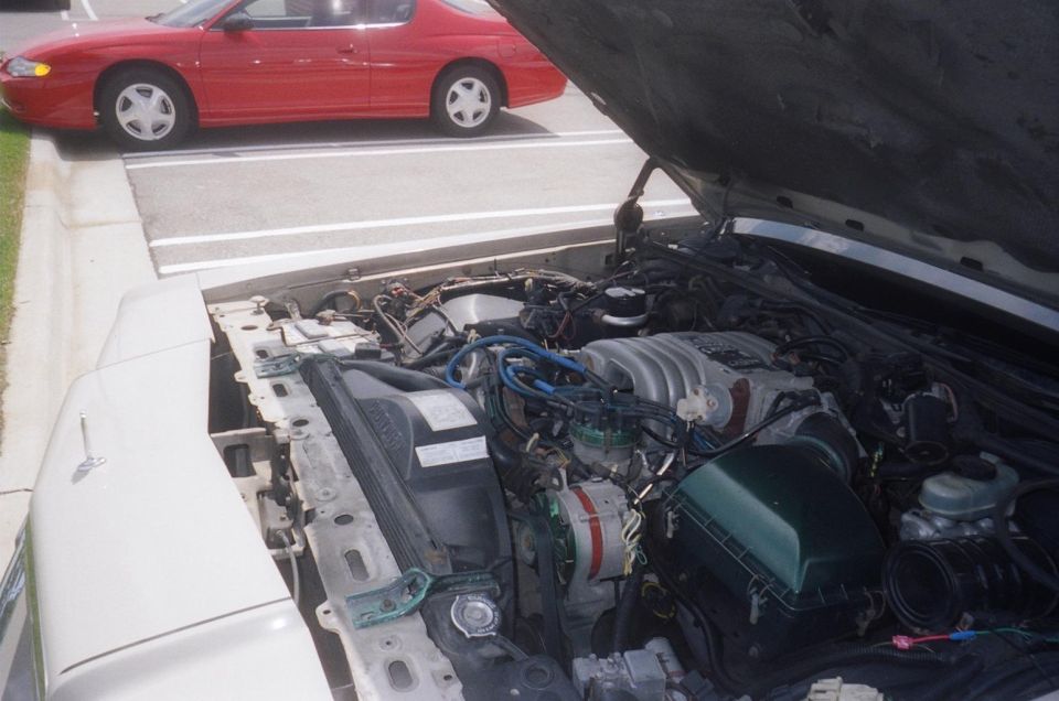 Engine bay of a white sedan with a red coupe parked behind it