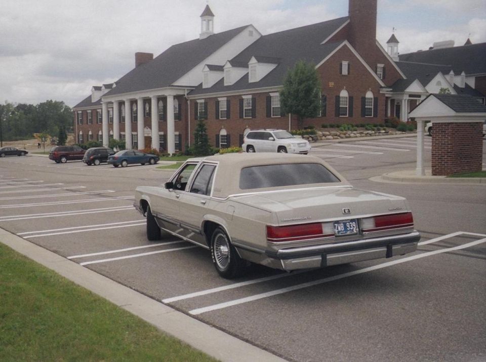 Rear view of a tan Mercury sedan before a brick building
