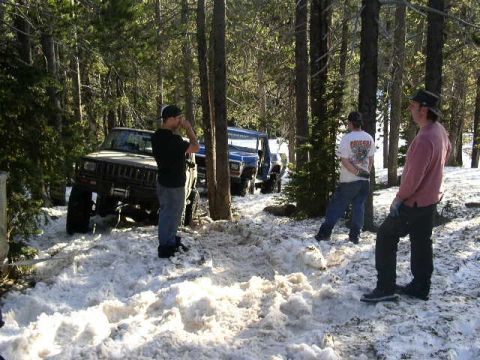 1979 Ford Bronco - Several people stand around a Jeep Cherokee XJ stuck in the snow in a wooded area.