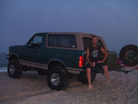 1996 Ford Bronco - Green and tan two-tone lifted Ford Bronco with a matching hardtop parked on beach sand at dusk with the ocean behind it. It rides on chrome…