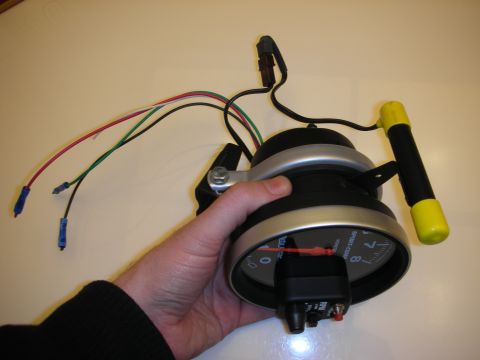 1998 Ford Crown Victoria - hand holds a pedestal-mount tachometer with yellow visor and exposed red, green and black wiring.