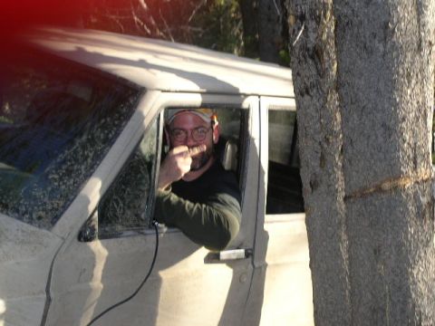 1979 Ford Bronco - A man gestures with his middle finger while looking out the window of a vehicle, partially obscured by a tree.