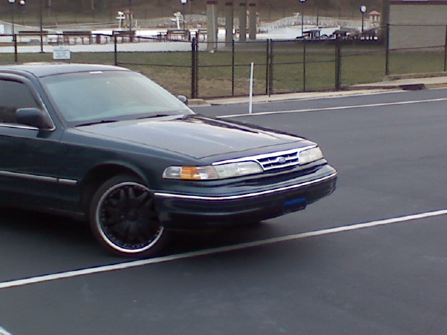 Dark green Crown Victoria sedan with black aftermarket wheels parked in an empty lot