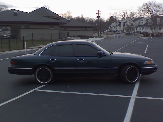 Dark sedan parked in a lot, side view. Black rims and tinted windows