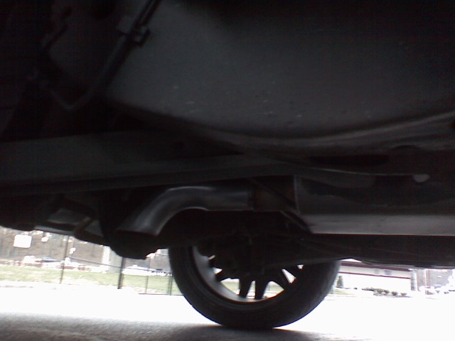 Underbody view of a car showing exhaust pipe, muffler, and rear wheel from ground level