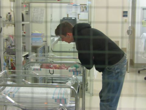 1987 Suzuki Samurai - A person leans over to view a newborn baby in a hospital bassinet, surrounded by medical equipment.
