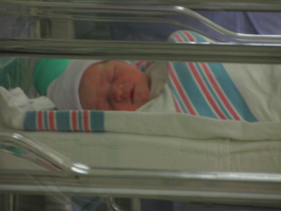 Newborn baby sleeping in a bassinet, wearing a hat and wrapped in a striped blanket