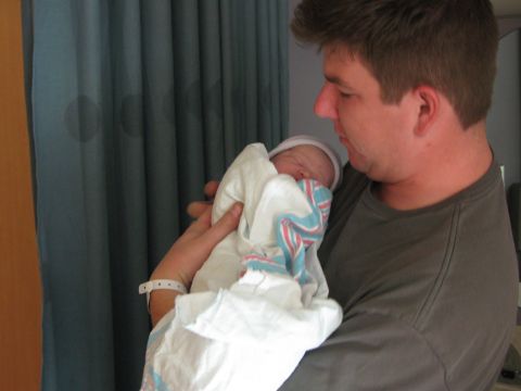 1987 Suzuki Samurai - A man holds his newborn baby, wrapped in a blanket and wearing a hat.